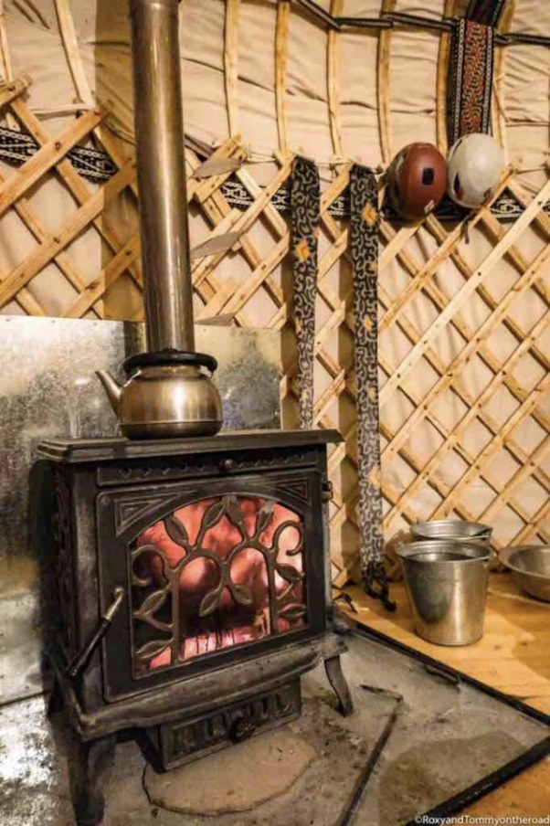 Wood-burning stove with a copper kettle and a glowing fire inside the yurt