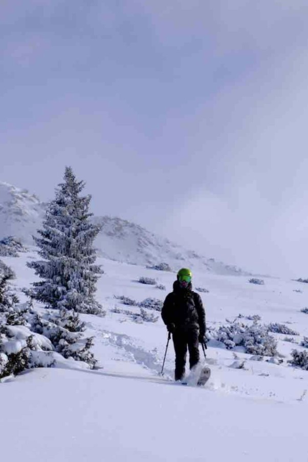 Snowboarder walking through deep fresh snow among frosted pines near the yurt
