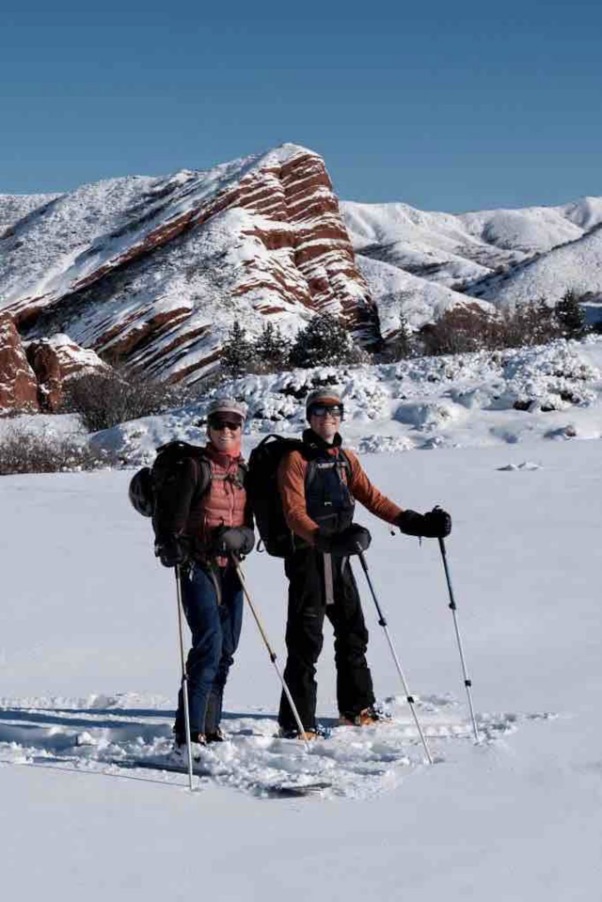 Two splitboarders standing on the snow in front of the tilted red Seven Bulls rock