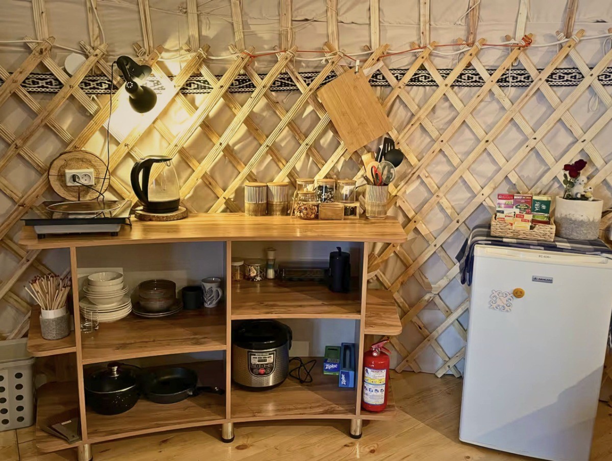The yurt kitchen with a kettle, hot plate, dishes, rice cooker, pots and a mini fridge